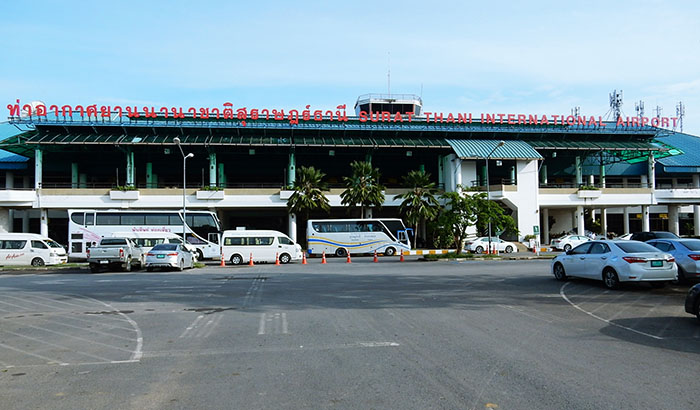 Frontal view of Surat Thani International Airport's entrance with parked vehicles and clear signage.