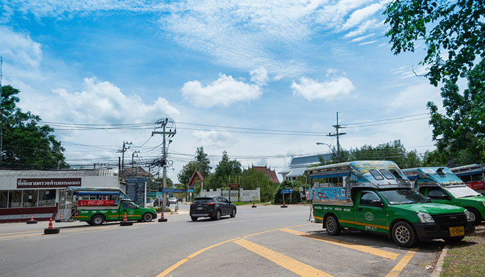 Green songthaew taxis parked at Khao Takiab in Hua Hin, ready to transport passengers around town. The scene includes a clear blue sky, power lines, and a small building in the background.