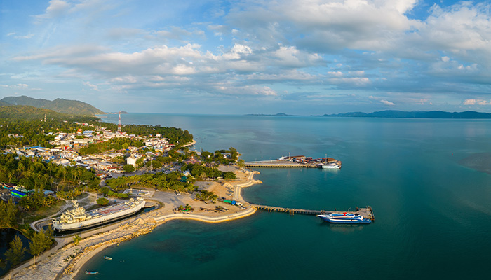 Aerial view of Thong Sala ferry harbor and town on Ko Pha Ngan, with Ko Samui in the background.